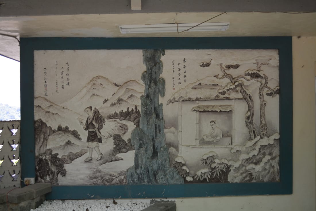 廟旁涼亭牆上的灰泥浮雕，雪景山水裡一名挑擔的旅人走在路上，另一側屋窗內有人伏案，旁有題字與落款。