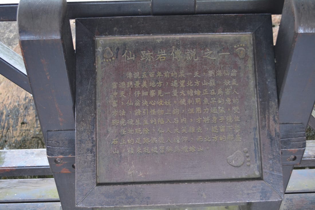 步道旁木架上的解說牌，題為「仙跡岩傳說之一」，四角刻著腳印圖案，牌面已隨風雨變色。